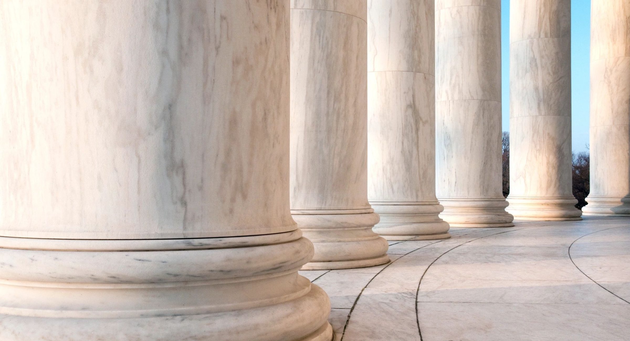 Close-up view of tall marble columns in a row under a blue sky, warm white and grey tones, stately mood.